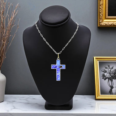Necklace with a blue cross pendant on a black bust against a gray wall.